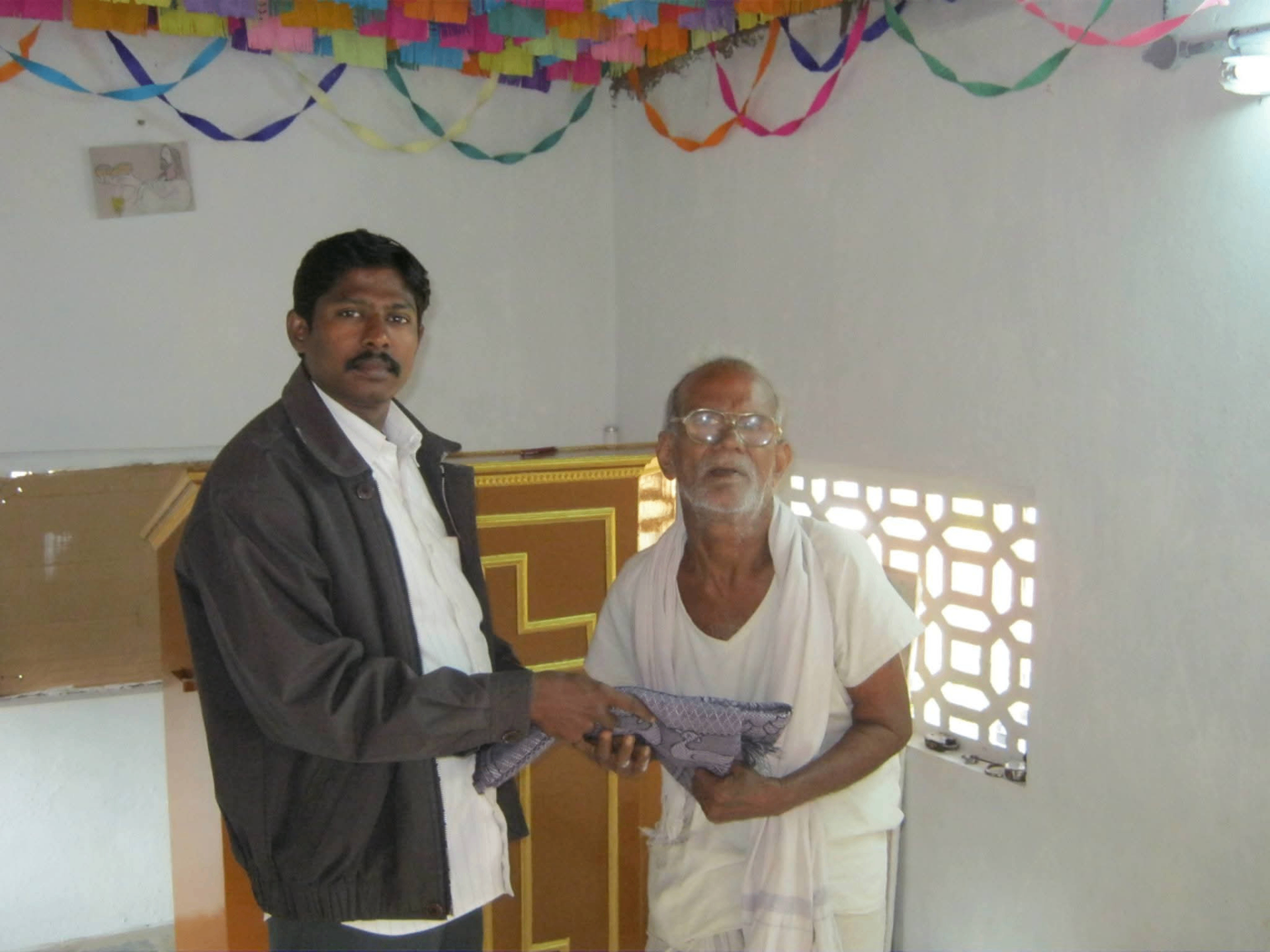 Pastor presenting a gift shawl to an elderly leprosy patient