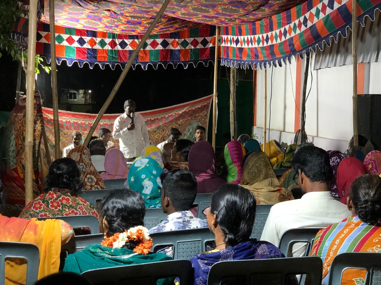 Pastor preaching under a colourful pandal to a seated congregation
