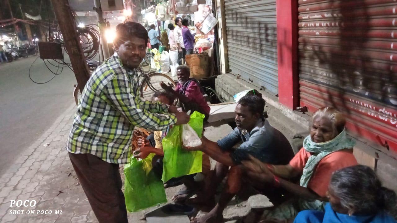 Ministry worker handing food bags to homeless elders on a footpath at night